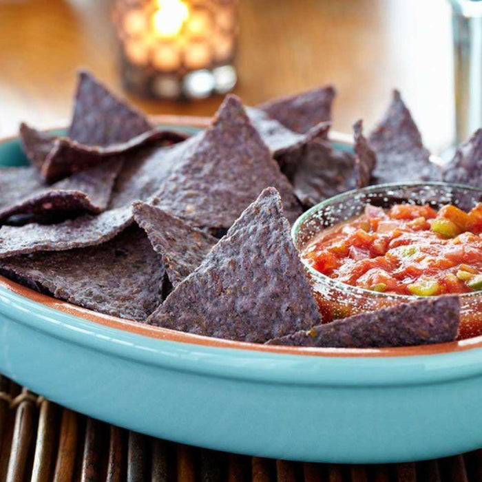 Blue corn tortilla chips with salsa in a teal bowl on a wooden surface.