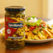 Jar of San Marcos jalapeño peppers next to a plate of nachos with toppings on a wooden surface.