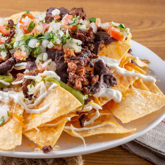 Platter of loaded white nachos with meat, cheese, and vegetables on a wooden table.