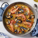 Paella with shrimp and mussels in a large pan on a white table.