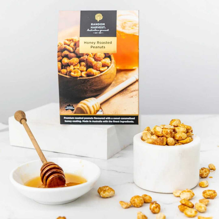 Honey roasted peanuts in a bowl with a honey dipper and packaging on a white background