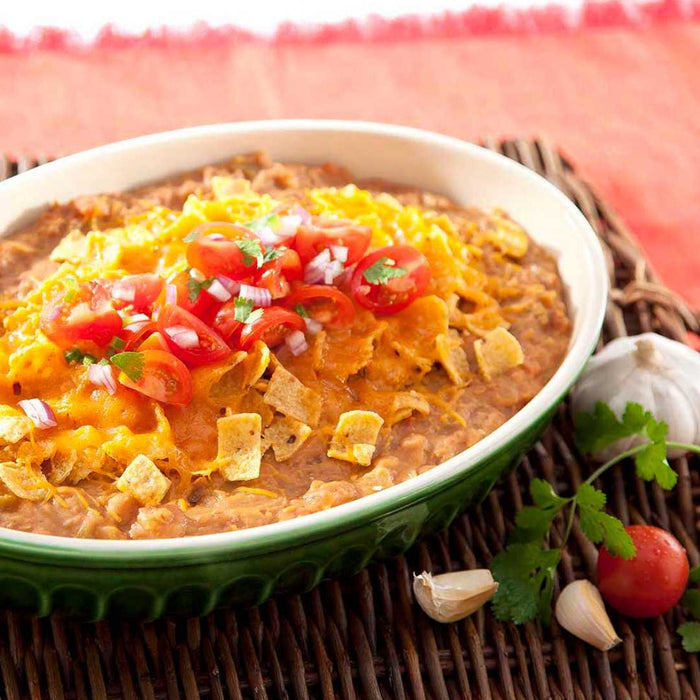 Bowl of refried pinto beans, chorizo, chili with cheese, tomatoes, and onions on a woven mat.