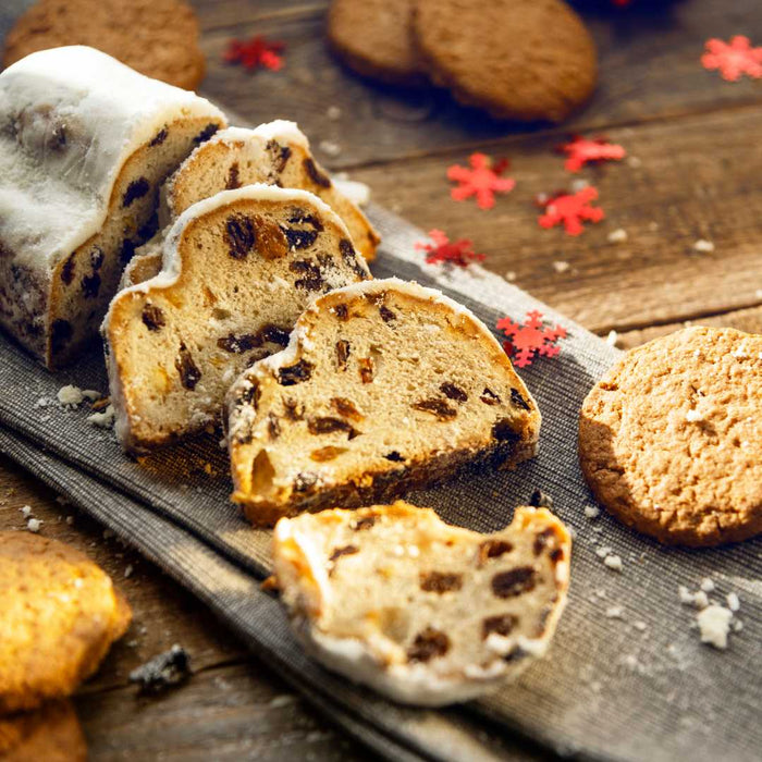 Sliced stollen with raisins on a wooden board with cookies and red flower decorations.