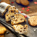 Sliced stollen with raisins on a wooden board with cookies and red flower decorations.